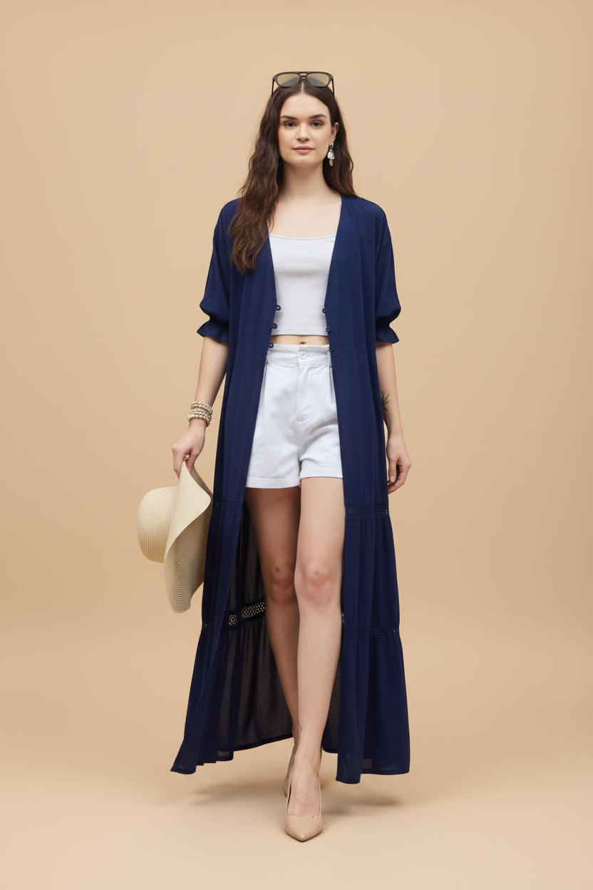 Woman wearing a long navy cardigan over a white outfit, holding a hat on a white background
