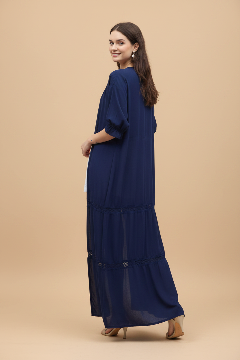 Woman wearing a long navy cardigan over a white outfit, holding a hat on a white background