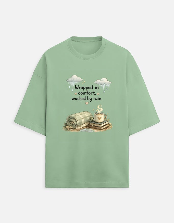 Snuggle Spot sage green oversized terry-knit unisex t-shirt with a cozy graphic print of a blanket, books, and coffee.